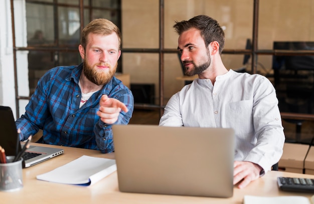 Equipaggi indicare il dito al computer portatile del suo collega nel luogo di lavoro