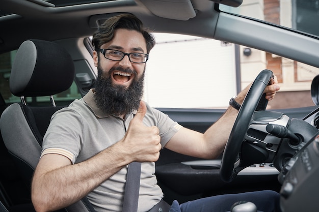 Equipaggi l'autista sorridente felice che mostra i pollici su che conducono l'automobile sportiva