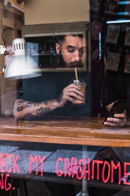 Equipaggi la bevanda bevente del cioccolato mentre utilizzano il telefono cellulare nel caffè