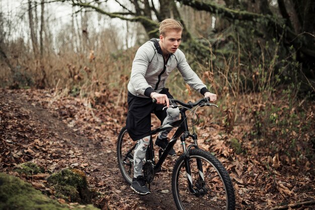 Equipaggi la bicicletta di guida nella foresta durante l&#39;autunno