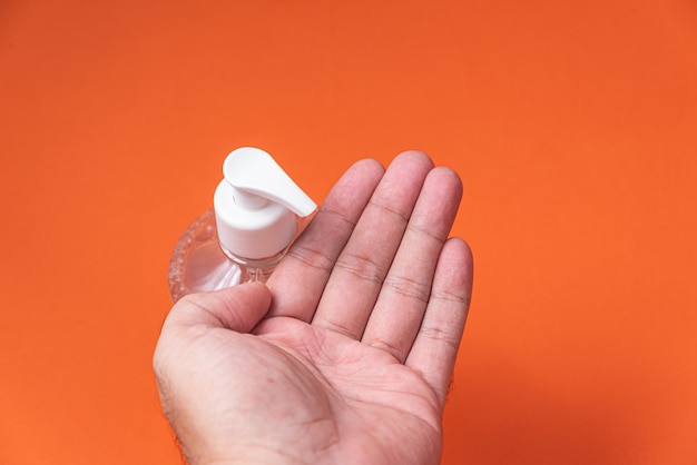 Equipaggi la mano in contenitore con il gel dell'alcool sulla parete arancio