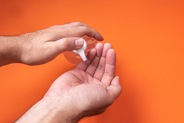 Equipaggi la mano in contenitore con il gel dell'alcool sulla parete arancio