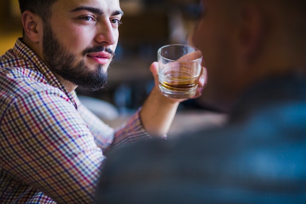 Equipaggi la seduta con il suo amico che tiene vetro di whiskey