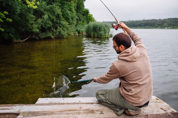 Equipaggi la seduta sul pilastro che pesca il pesce con la canna da pesca