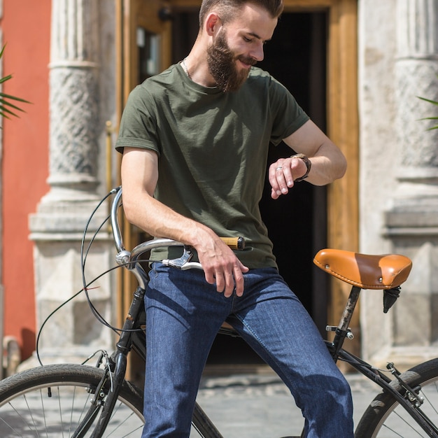 Equipaggi la seduta sulla bicicletta che esamina il tempo sull&#39;orologio