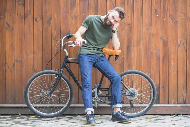 Equipaggi la seduta sulla bicicletta contro la parete di legno