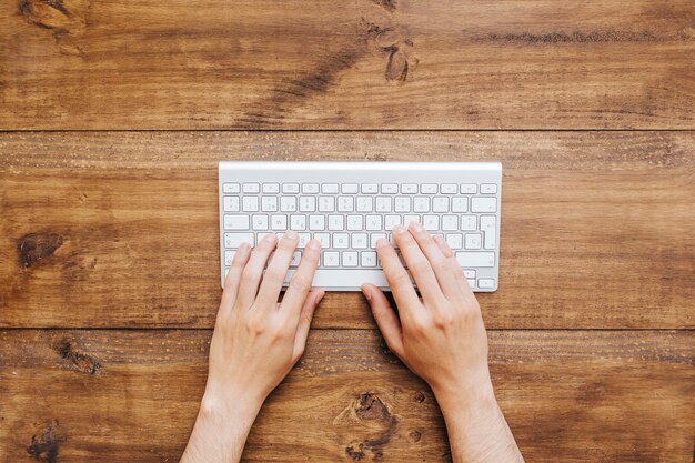 Equipaggi le mani che lavorano alla tastiera sopra fondo di legno