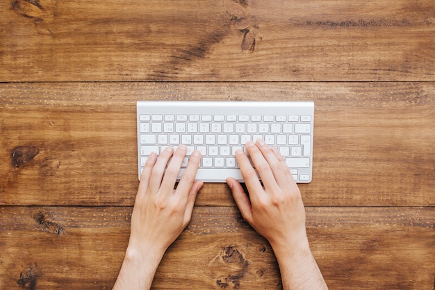 Equipaggi le mani che lavorano alla tastiera sopra fondo di legno