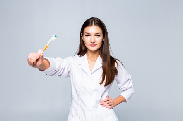 Erba medica sorridente della donna con le parentesi graffe con i grandi denti che tengono spazzolino da denti, isolato sulla parete bianca