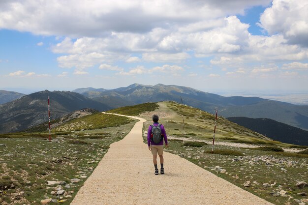 Escursionista con uno zaino che cammina attraverso una strada su una collina ricoperta di verde - concetto di successo