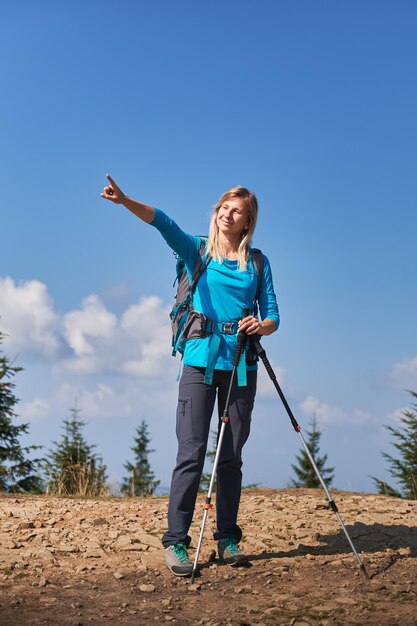 Escursionista femminile in piedi sulla strada di montagna e che punta a qualcosa