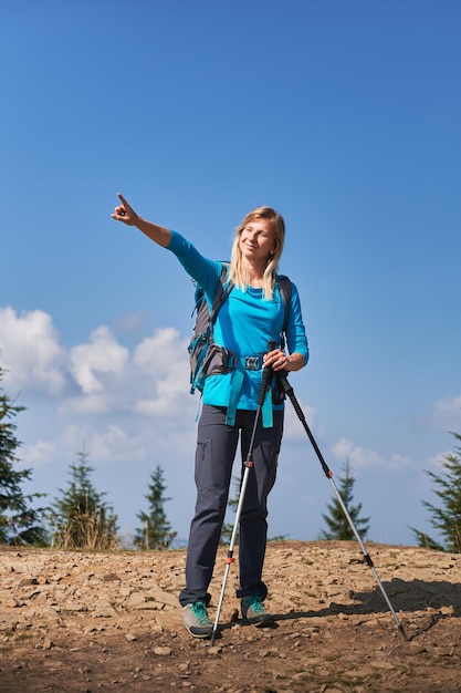 Escursionista femminile in piedi sulla strada di montagna e che punta a qualcosa