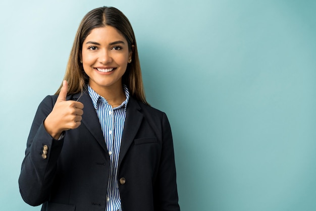 Esecutivo femminile ispanico che gesturing i pollici in su contro il fondo isolato