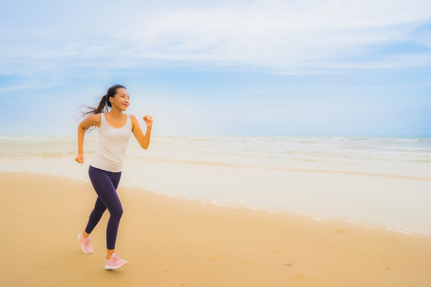 Esercizio asiatico della donna di bello giovane sport del ritratto eseguendo e pareggiando sulla spiaggia e sul mare all&#39;aperto della natura