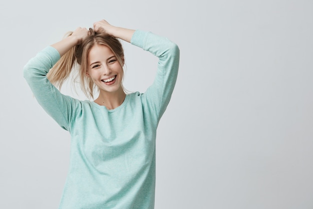 Espressioni ed emozioni del volto umano. La giovane bella femmina positiva con capelli lisci biondi tinti in coda di cavallo si è vestita in abbigliamento casual