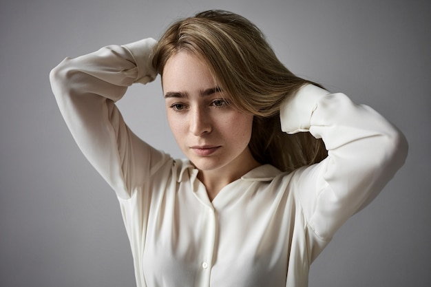 Espressioni facciali umane e reazione. Ritagliata colpo di bella giovane donna di affari stanca lentigginosa in abbigliamento formale che regola i capelli, con sguardo frustrato pensieroso, pensando a problemi di lavoro