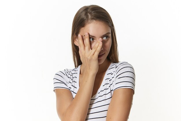 Espressioni facciali umane, emozioni, reazioni e sentimenti. Vista orizzontale della splendida giovane femmina caucasica spaventata, distogliendo lo sguardo e coprendosi il viso con il palmo, avendo uno sguardo terrorizzato