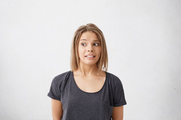 Espressioni facciali umane, emozioni, sentimenti, atteggiamento e reazione. Primo piano del volto di una ragazza divertente con l'acconciatura bob che guarda lontano, sentendosi confuso, mantenendo un silenzio imbarazzante in una situazione imbarazzante