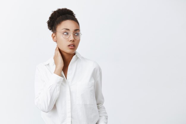 Essere un grande capo faticoso. Elegante e tenero impiegato afroamericano femminile in occhiali e camicia bianca, toccando il collo e guardando con espressione stanca sognante a destra, sentendo dolore al collo