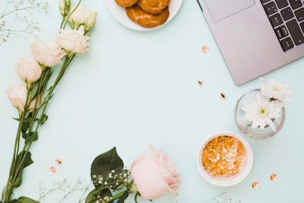 Eustoma e fiori di rosa con biscotti; puntina d&#39;oro; e laptop su sfondo blu pastello