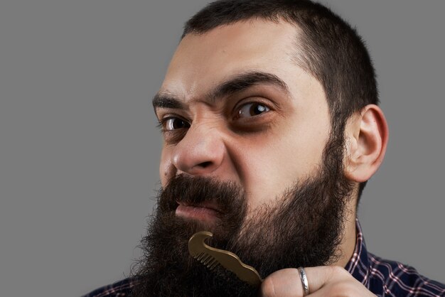 Faccia buffa dell'uomo brutale che pettina la sua grande barba. Concetto di negozio di barbiere.