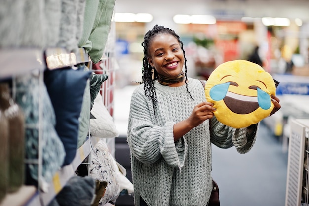 Faccia con lacrime di gioia emoji concetto LOL Donna africana con cuscino che ride ad alta voce in un moderno negozio di arredamento per la casa