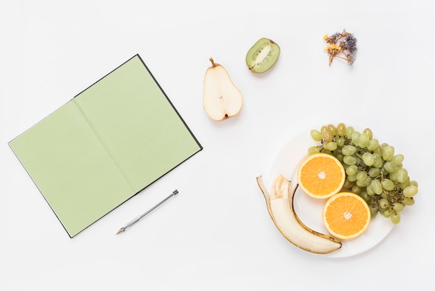 Faccina sorridente fatta con frutta sul piatto; libro e penna isolati su sfondo bianco