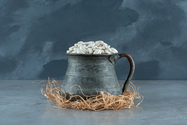 Fagioli bianchi in un vaso etnico metallico su erbe secche. Foto di alta qualità