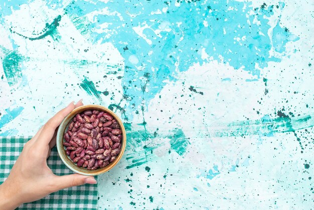 Fagioli crudi di vista dall'alto all'interno del piatto rotondo sul chicco di fagioli crudi di cibo da scrivania azzurro