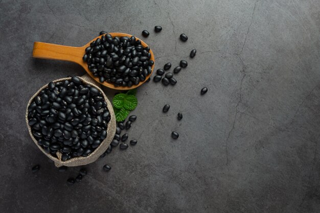 fagiolo nero in un piccolo cucchiaio di legno posto accanto al sacco pieno di fagioli neri
