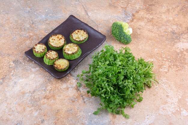 Fagottino di coriandolo, pezzo di broccoli e un piatto di zucchine fritte su superficie di marmo