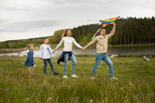 Famiglia a tutto campo che gioca con l'aquilone arcobaleno