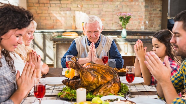 Famiglia al tavolo che prega prima di mangiare