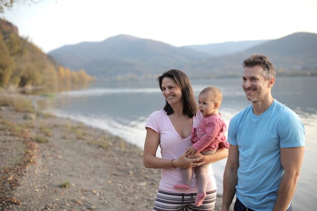 Famiglia allegra con un bambino piccolo in piedi vicino a un lago circondato da colline sotto la luce del sole