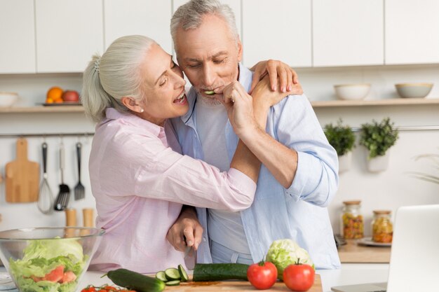 Famiglia amorosa divertente matura delle coppie che per mezzo del computer portatile e cucinando insalata