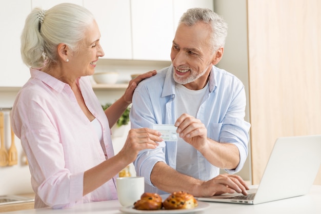 Famiglia amorosa matura allegra delle coppie facendo uso della carta di credito della tenuta del computer portatile