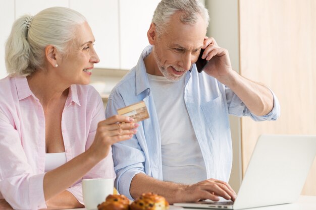 Famiglia amorosa matura sorridente delle coppie facendo uso della carta di credito della tenuta del computer portatile.