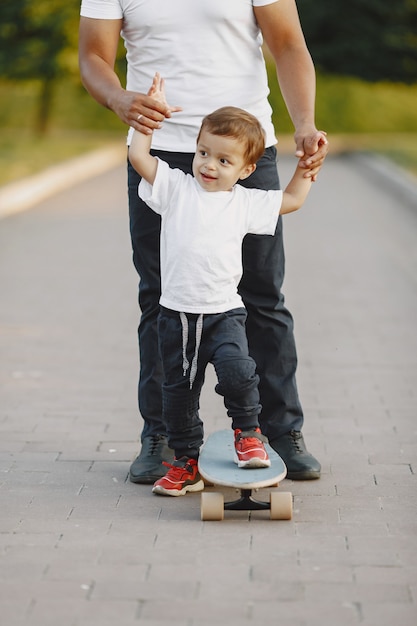 Famiglia asiatica in un parco. Uomo in una maglietta bianca. Il padre insegna al figlio a cavalcare uno skate.