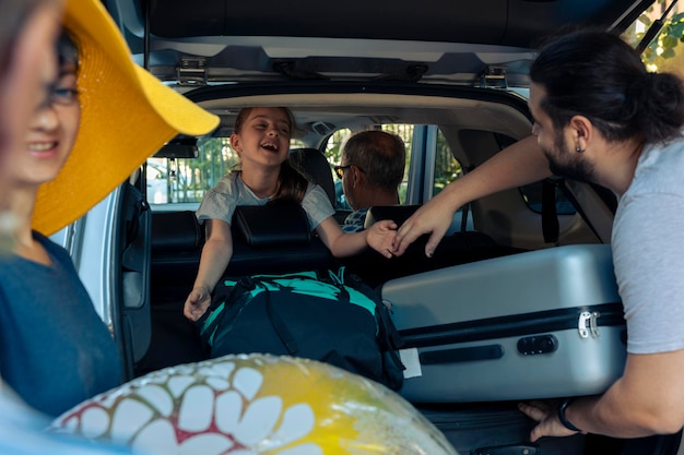 Famiglia caucasica che viaggia in vacanza in auto, mettendo trolley e borse nel bagagliaio del veicolo. Genitori e nonni che partono in vacanza con la bambina, preparando la valigia e i bagagli.