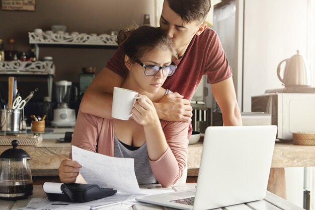 Famiglia caucasica infelice che ha problemi economici. Giovane di supporto che cerca di rallegrare la moglie preoccupata con gli occhiali che si sente stressato, affrontando un problema finanziario