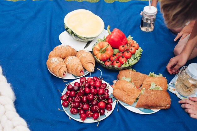 Famiglia che fa picnic sulla coperta croissant e panini fatti in casa con limonata L'uomo sta tagliando un'anguria gialla