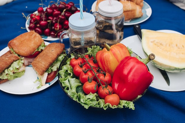 Famiglia che fa picnic sulla coperta croissant e panini fatti in casa con limonata L'uomo sta tagliando un'anguria gialla