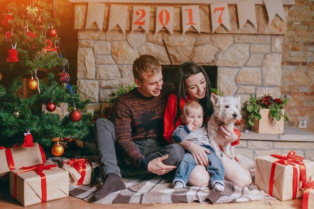 Famiglia che si siede davanti al camino con il loro bambino e il loro cane e un albero di Natale