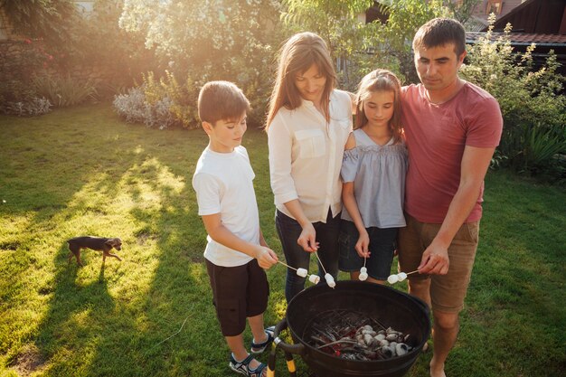 Famiglia che sta barbecue vicino e che arrostisce caramella gommosa e molle in parco