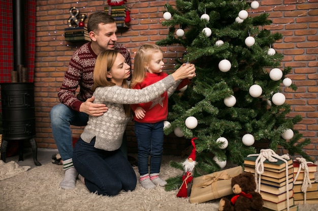 Famiglia con i giocattoli d&#39;attaccatura della piccola figlia su un albero di Natale