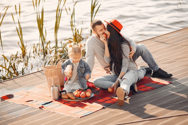 Famiglia con la piccola figlia che si siede vicino all'acqua in un parco di autunno