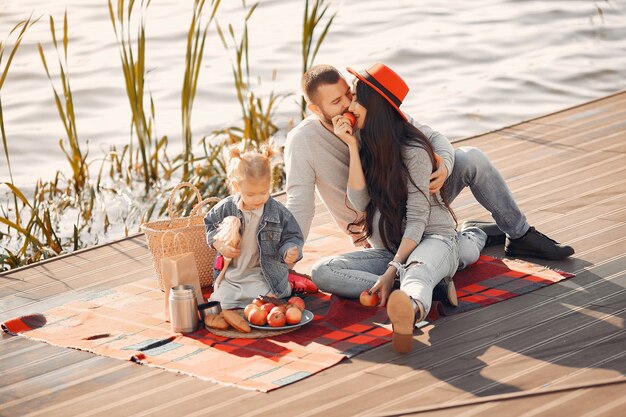 Famiglia con la piccola figlia che si siede vicino all'acqua in un parco di autunno