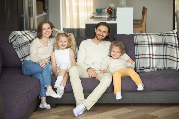 Famiglia di quattro felice che si siede sul sofà che guarda l&#39;obbiettivo