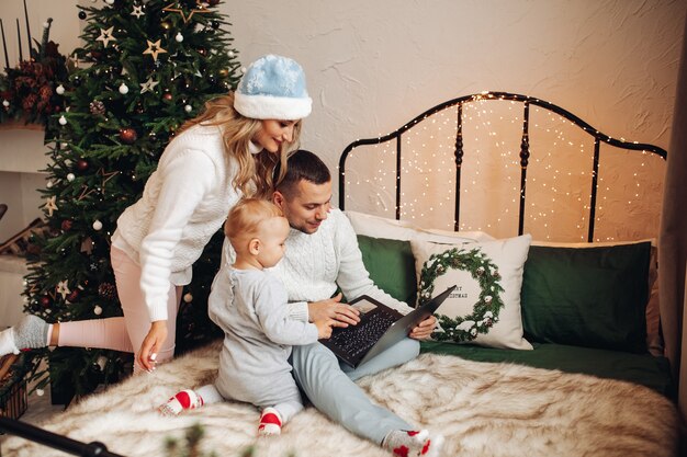 Famiglia felice che celebra il Natale sul letto e utilizzando il computer portatile per la comunicazione con i parenti.