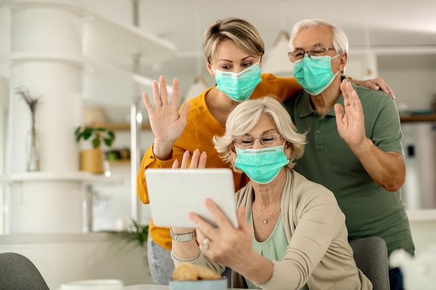 Famiglia felice che saluta mentre fa una videochiamata sul touchpad a casa durante la pandemia di COVID19